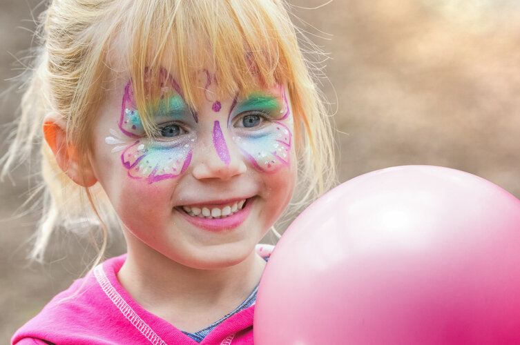 Kind mit blonden Haaren und geschminktem Gesicht und Luftballon