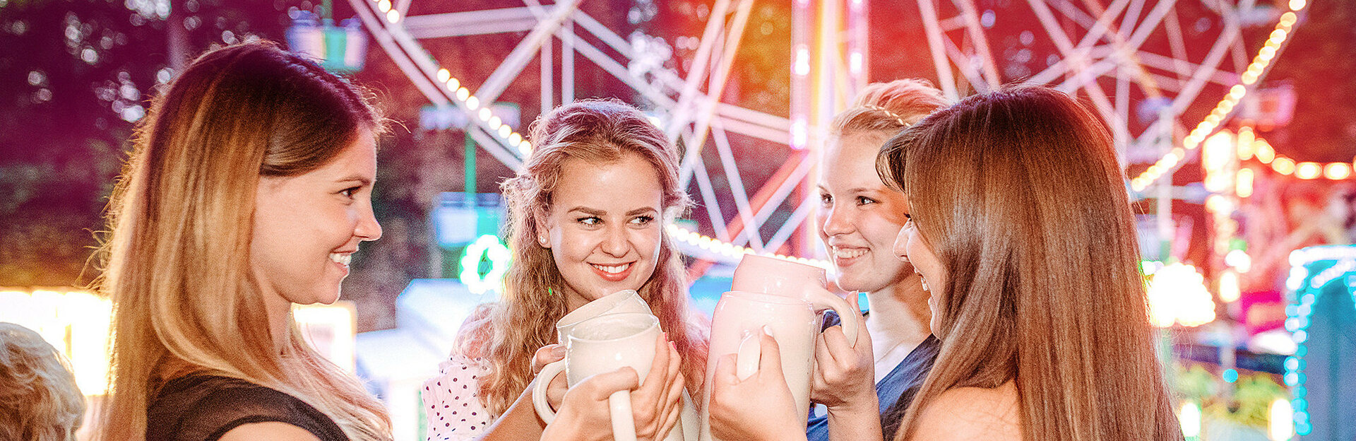 Drei junge Frauen stoßen mit Bier am Annafest vor dem Riesenrad an