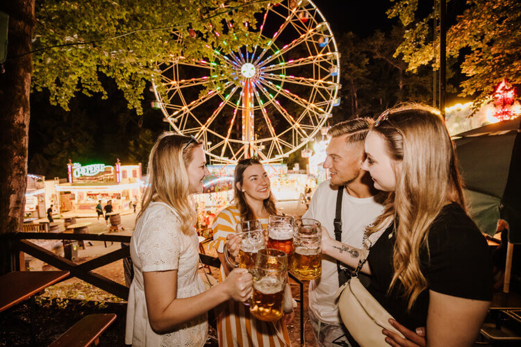 Annafest bei Nacht: Drei junge Frauen und ein junger Mann stoßen mit Bierkrügen vor dem Riesenrad an